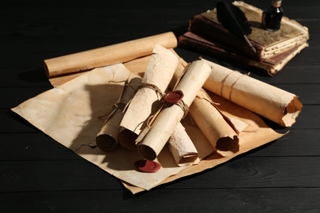Many old rolled scrolls and books on black wooden table, closeup
