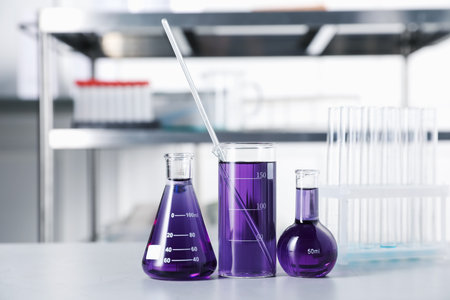Different laboratory glassware with purple liquid on light table indoorsの写真素材