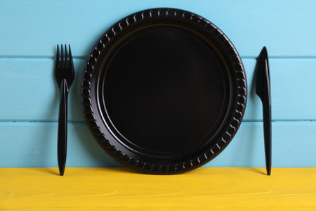Set of disposable plastic tableware on yellow wooden table against light blue background, closeup. Space for textの写真素材