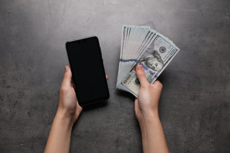 Woman with money and smartphone at gray table, top viewの写真素材