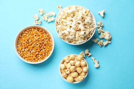 Tasty popcorn and dry kernels in bowls on light blue background, flat layの写真素材