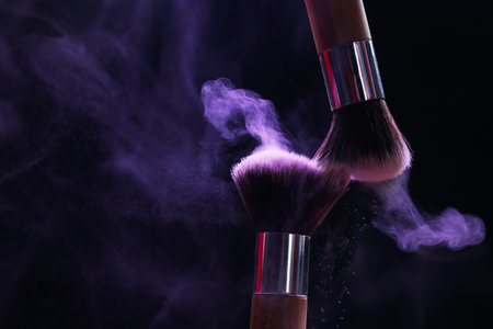 Makeup brushes with purple eye shadow in neon lights on black background, closeup. Space for textの写真素材