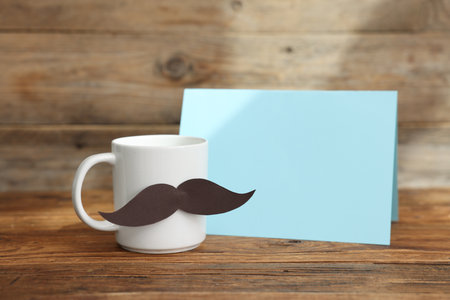 Happy Father's Day. Cup with mustache and card on wooden table. Space for textの写真素材
