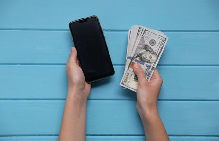 Woman with money and smartphone at blue wooden table, top viewの写真素材