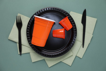 Set of disposable plastic tableware and paper napkins on green background, flat layの写真素材