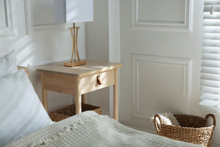 Bedside table with lamp near bed indoors
