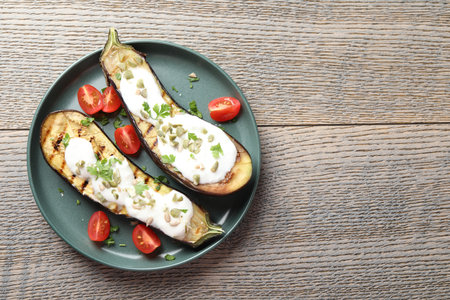 Slices of grilled eggplant with pumpkin seeds, tomatoes and yoghurt on wooden table, top view. Space for textの写真素材