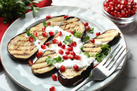 Slices of grilled eggplant with pomegranate seeds and yoghurt on white marble table, closeupの写真素材