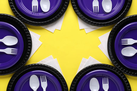 Frame of disposable plastic tableware and paper napkins on yellow background, flat lay. Space for textの写真素材