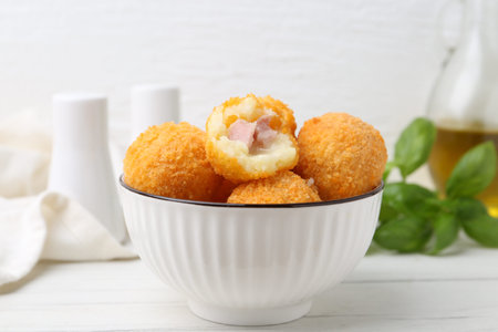 Delicious fried croquette balls in bowl on white wooden table, closeup