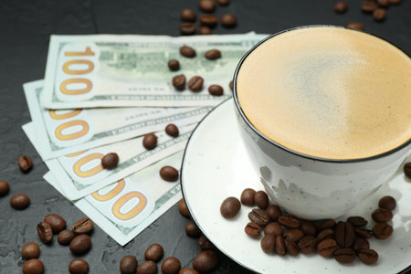 Cup of aromatic coffee, dollar banknotes and roasted beans on dark textured table, closeupの写真素材