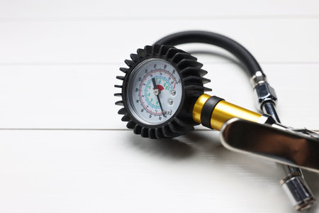 One tire inflation gun with gauge on light wooden table, closeup