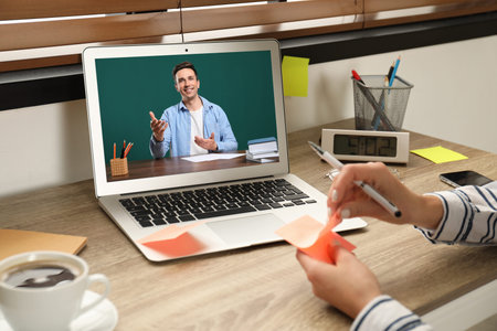 E-learning concept. Student having online video chat with teacher via laptop at desk, closeup