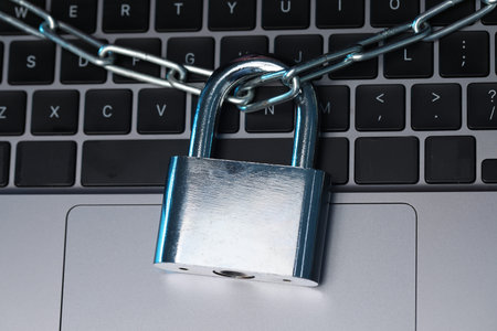 Cyber safety. Metal padlock with chain on laptop, above view