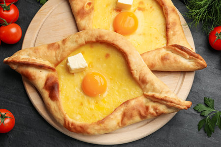 Tasty khachapuri with cheese, egg and other products on black table, flat layの写真素材
