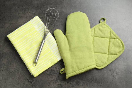 Green oven glove, potholder, towel and whisk on dark textured table, flat layの写真素材
