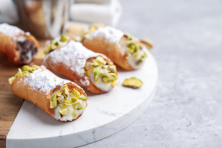 Delicious cannoli with ricotta cheese, pistachios and powdered sugar on grey marble table, closeup. Space for textの写真素材
