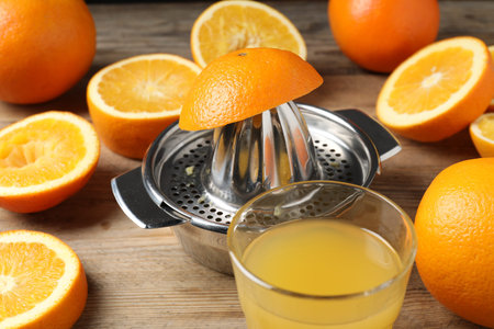 Freshly squeezed orange juice, fruits and juicer on wooden table, closeup