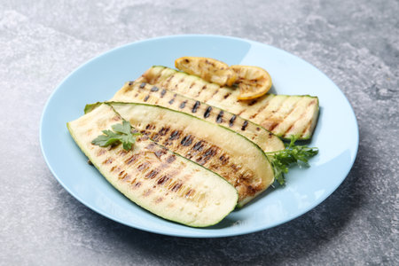 Delicious grilled courgette slices with parsley and lemon on gray textured table, closeupの写真素材