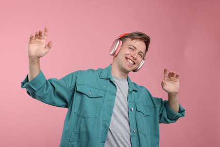 Happy man listening to music in headphones and dancing on pink background