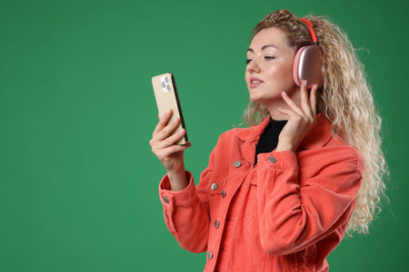 Happy woman with smartphone listening to music in headphones on green background. Space for text