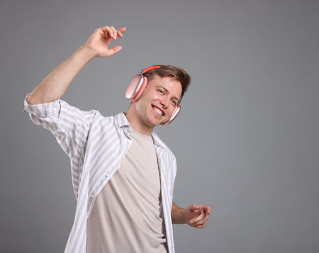 Happy man listening to music in headphones and dancing on grey backgroundの写真素材