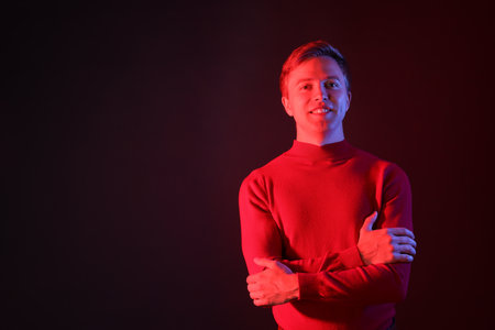 Portrait of smiling man with crossed arms in neon lights against dark background. Space for textの写真素材