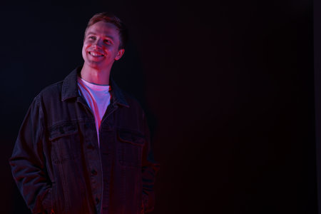 Smiling man in neon lights against black background. Space for text