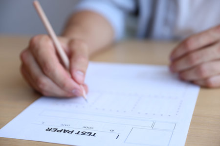 Student filling out multiple choice test at wooden table, closeup. Passing exam