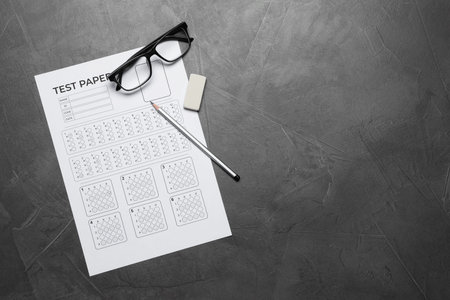 Student passing exam. Answer sheet, glasses, pencil and eraser on gray textured table, flat lay....