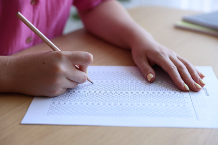 Student filling out multiple choice test at wooden table, closeup. Passing exam
