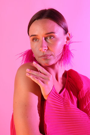 Beautiful woman wearing fur earrings in neon lights against pink backgroundの写真素材