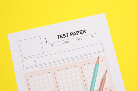 Answer sheet and pencils on yellow background, flat lay. Student passing exam
