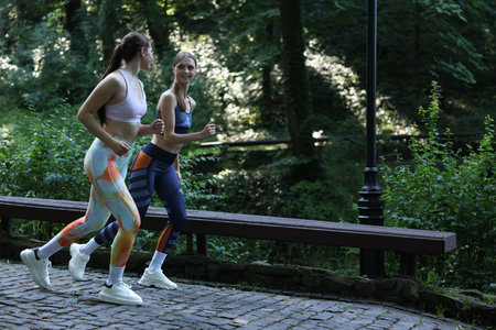 Young woman running with professional personal trainer outdoors. Space for text