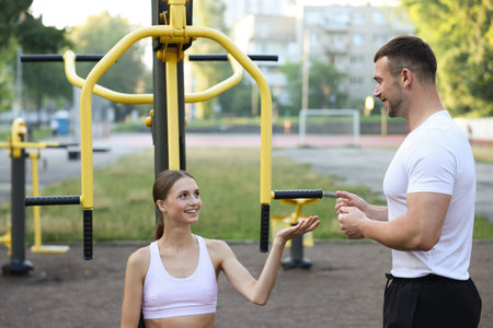 Young woman exercising with outdoor gym equipment with professional personal trainer outdoors