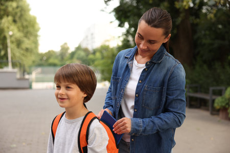 Mother putting book into son's backpack while taking him to school outdoorsの写真素材