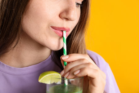 Woman drinking refreshing drink through straw on orange background, closeupの写真素材