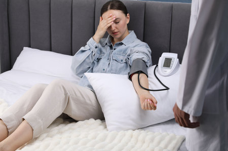 Doctor checking woman's heart rate and blood pressure via sphygmomanometer at home, closeup