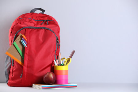 Red backpack with different stationery on table near light wall. Space for textの写真素材