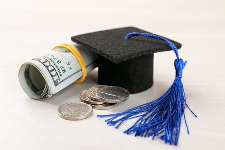 Scholarship. Graduate hat, dollar banknotes and coins on white table, closeup
