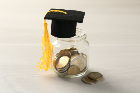 Scholarship. Jar with graduate hat and coins on white wooden table, closeupの写真素材