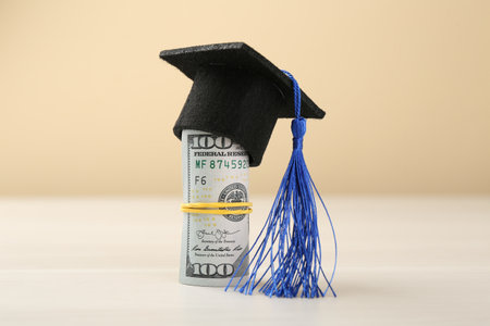 Scholarship. Graduate hat and dollar banknotes on white table against beige background, closeupの写真素材