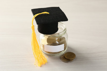 Scholarship. Jar with graduate hat and coins on white wooden table, closeupの写真素材