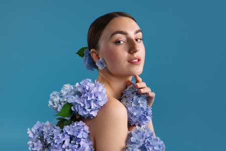 Beautiful young woman with hortensia flowers on blue backgroundの写真素材