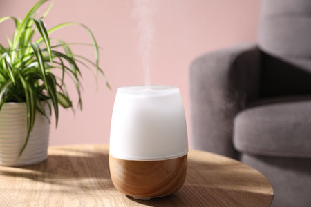 One stylish aroma lamp and houseplant on wooden table against pink wall, closeup