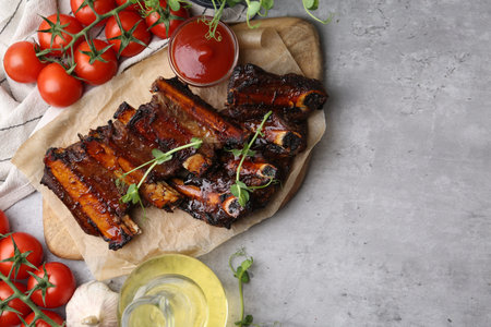 Roasted beef ribs with microgreens, tomatoes and other products on gray textured table, flat lay....