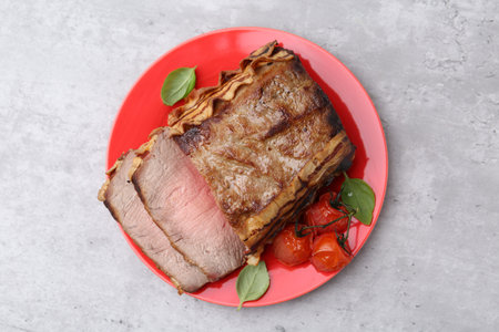 Delicious baked beef meat, tomatoes and basil on gray table, top view