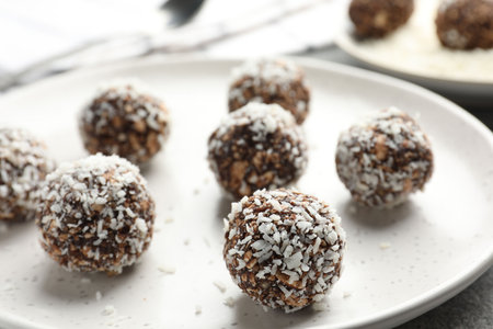Tasty chocolate candies with nuts and coconut flakes on gray table, closeup
