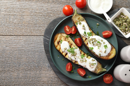 Slices of grilled eggplant with pumpkin seeds, tomatoes and yoghurt on wooden table, flat lay. Space for textの写真素材