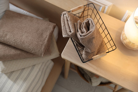 Stack of clean towels on bed linens and nightstand with metal basket at home, above viewの写真素材